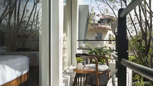 A balcony with a bed, a small table with a chair, and a view of a building with a tiled roof. - Kimpton Virgilio Polanco by IHG (Mexico City)