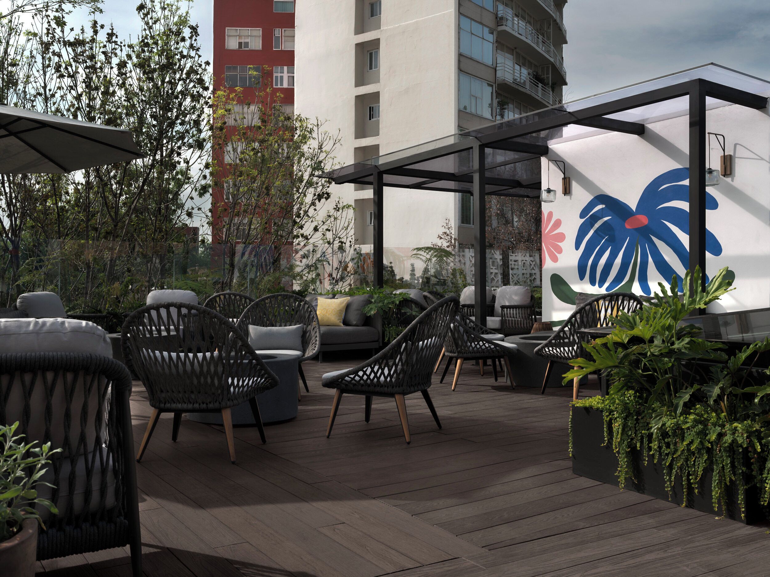 An outdoor seating area with wicker chairs and a sofa, surrounded by potted plants and a modern building in the background.