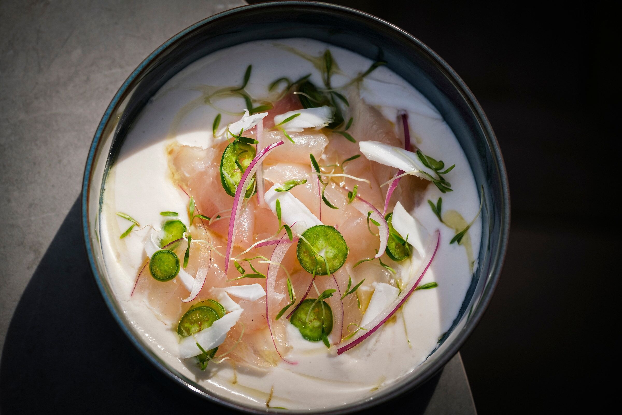 A bowl of food with thinly sliced fish, green herbs, and red onion slices.