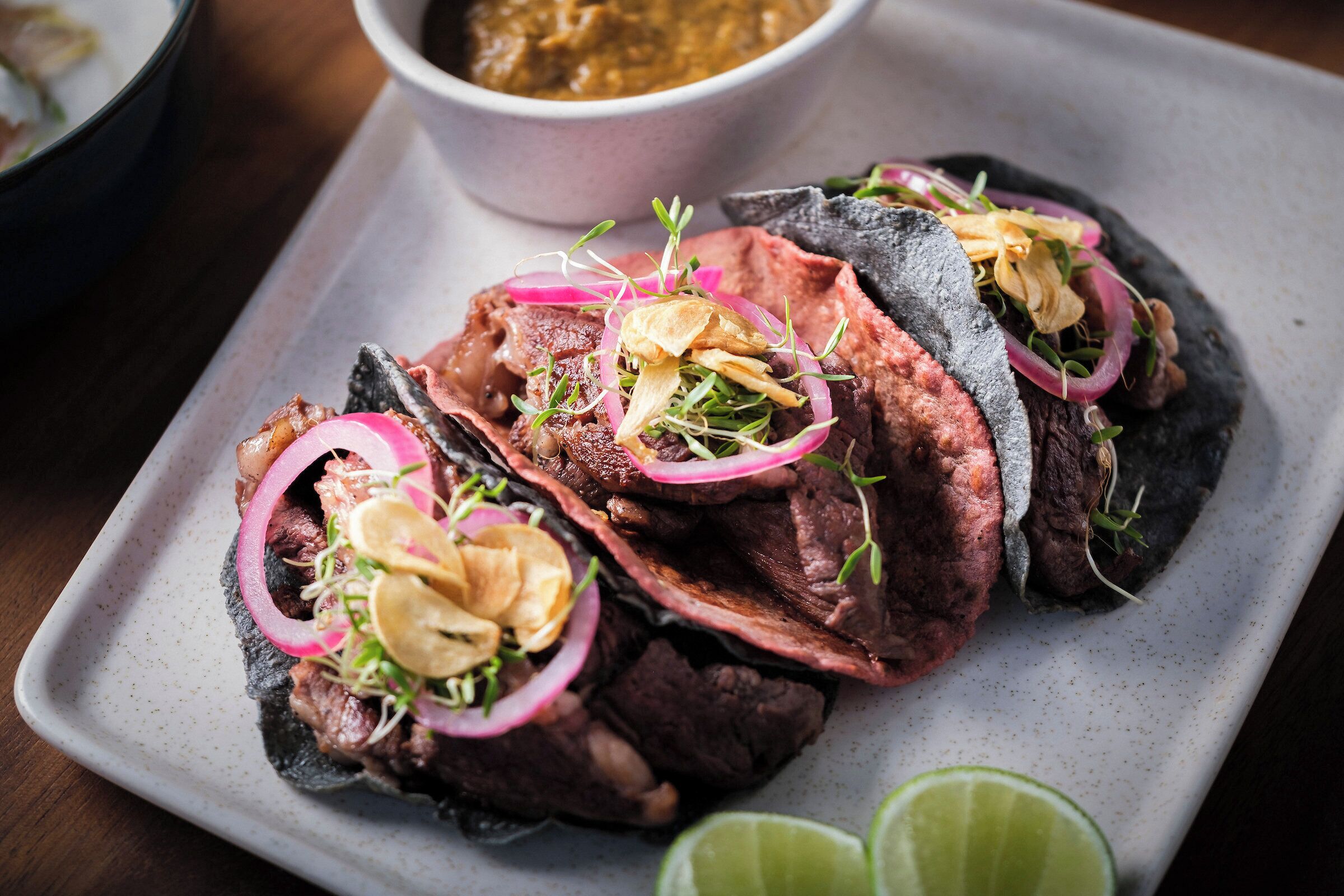A plate of tacos with meat, onions, and lime wedges.