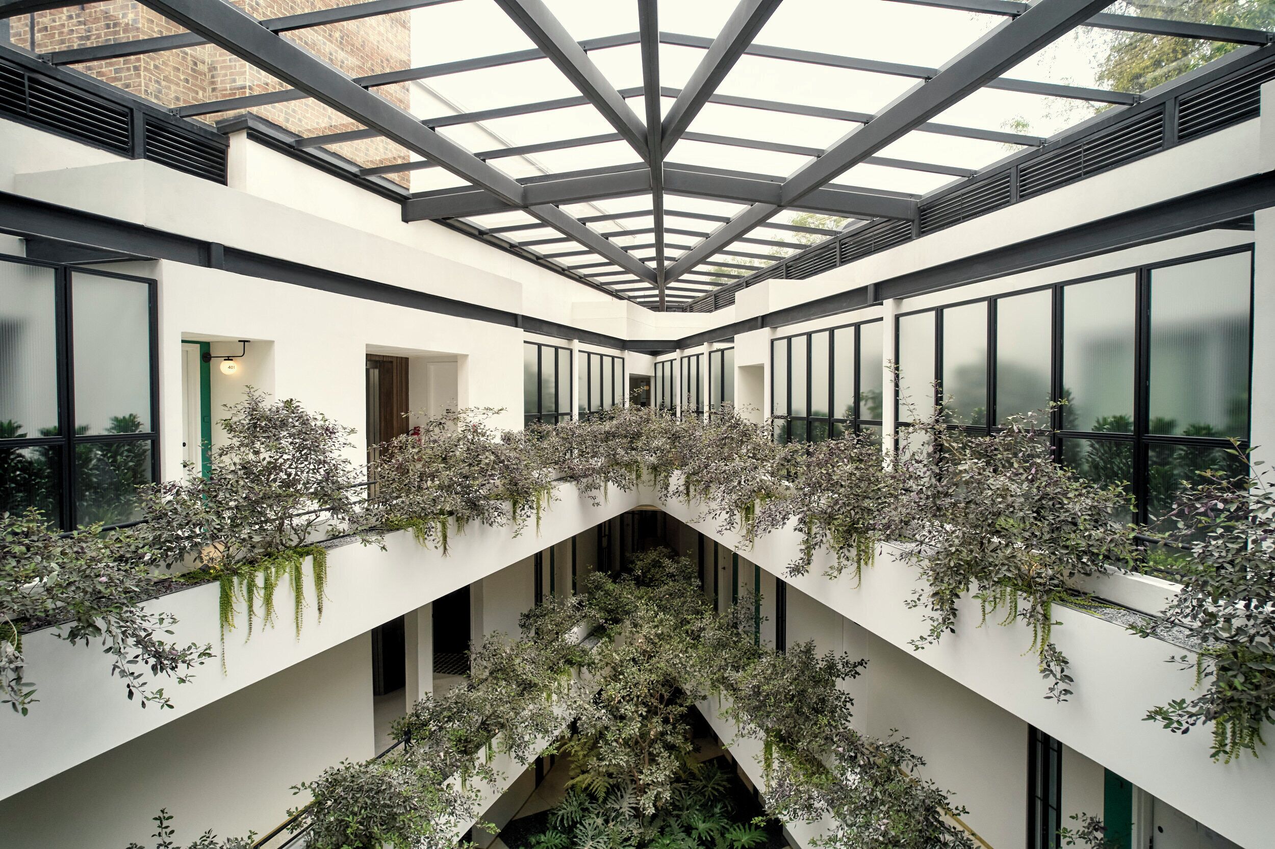 A modern building interior with a central atrium, glass ceiling, and extensive greenery.