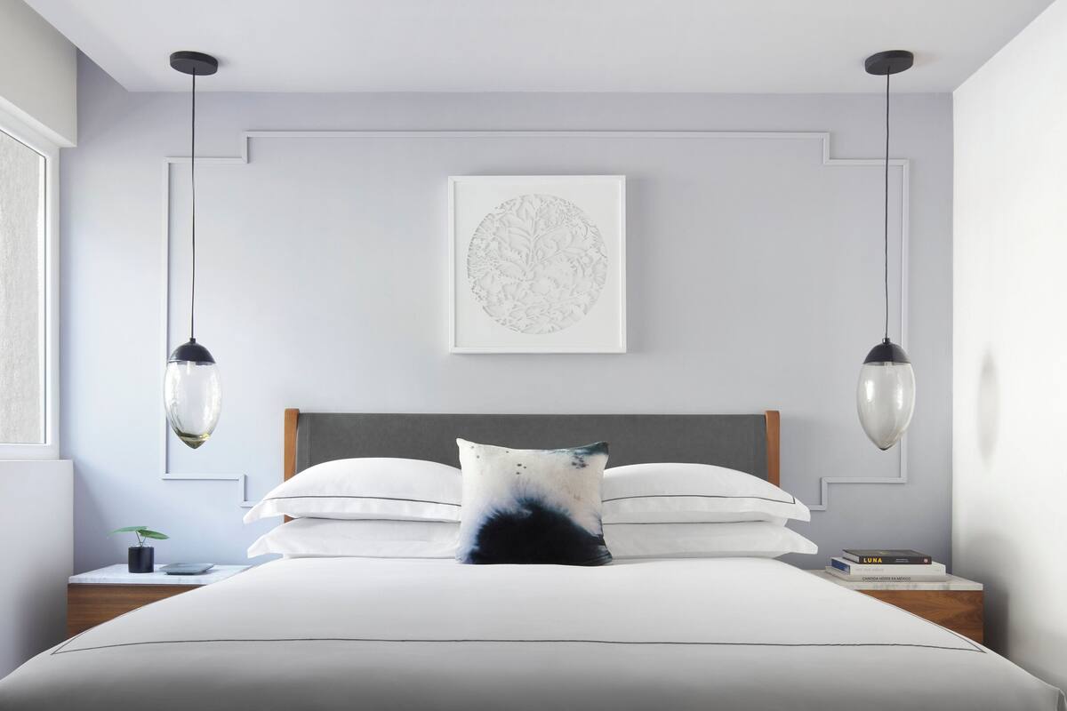 A modern bedroom with a large bed, two bedside tables, a framed artwork on the wall, and pendant lights.
