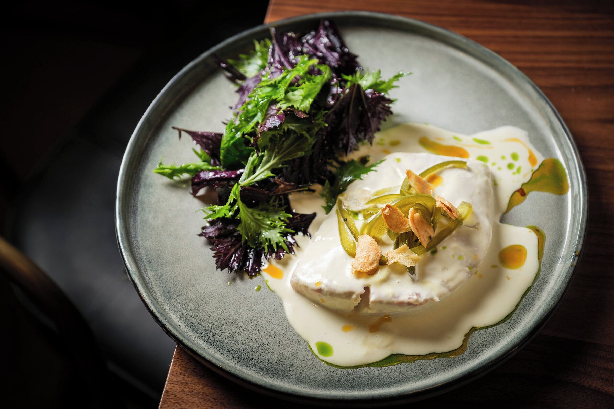 A plate with a creamy dish, garnished with herbs and pickles, on a dark plate.