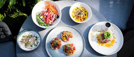 Una mesa con diversos platos, incluyendo mariscos y ensaladas, en un entorno al aire libre con vegetación de fondo.