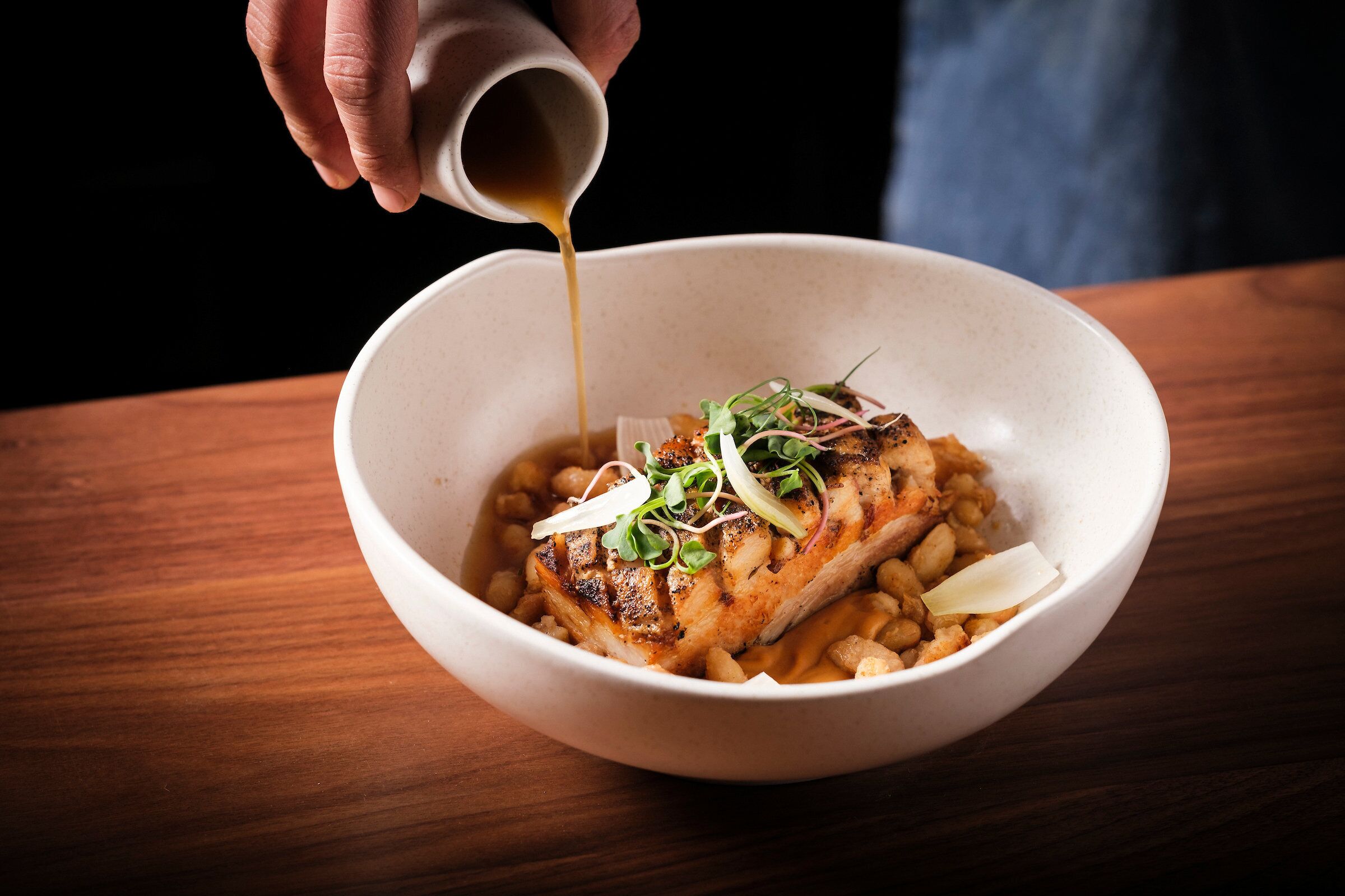A bowl of food with a hand pouring sauce over it.