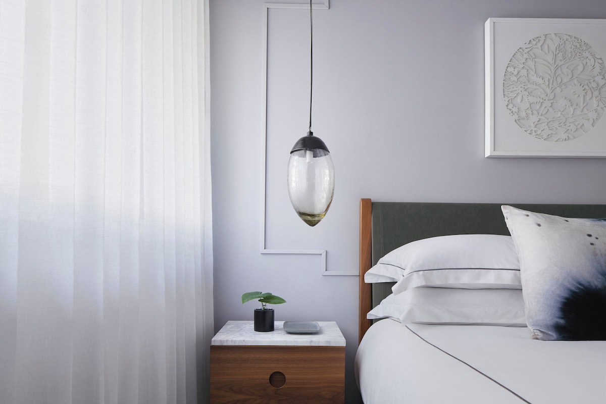 A neatly arranged bedroom with a bed, bedside table, and a hanging pendant light.