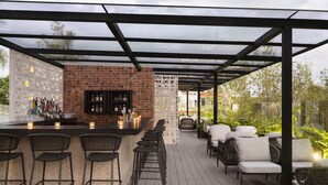 An outdoor bar area with a brick wall, bar stools, and a seating area with wicker chairs. - Kimpton Virgilio Polanco by IHG (Mexico City)