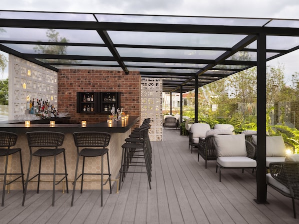 An outdoor bar area with a brick wall, bar stools, and a seating area with wicker chairs. - Kimpton Virgilio Polanco by IHG (Mexico City)