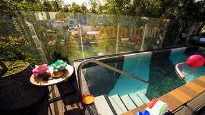 A glass-enclosed infinity pool with a wooden deck, a lounge chair, and a table with a bowl of snacks. - Kimpton Virgilio Polanco by IHG (Mexico City)