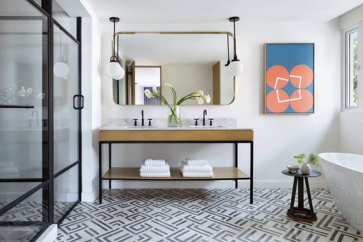 A modern bathroom with a marble sink, a wooden vanity, a large mirror, and a geometric patterned floor.