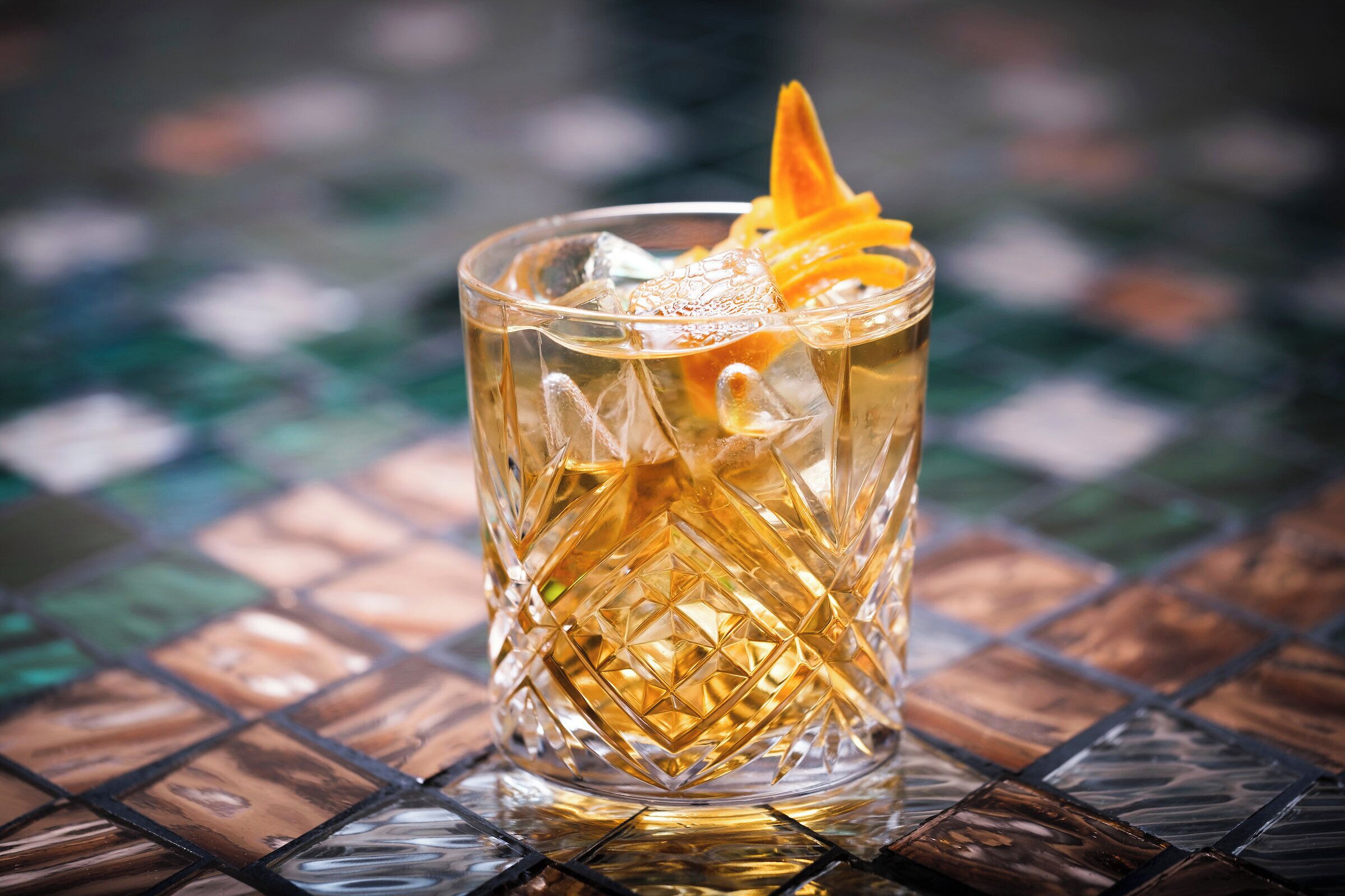 A glass with a textured pattern and a garnish, placed on a tiled surface.