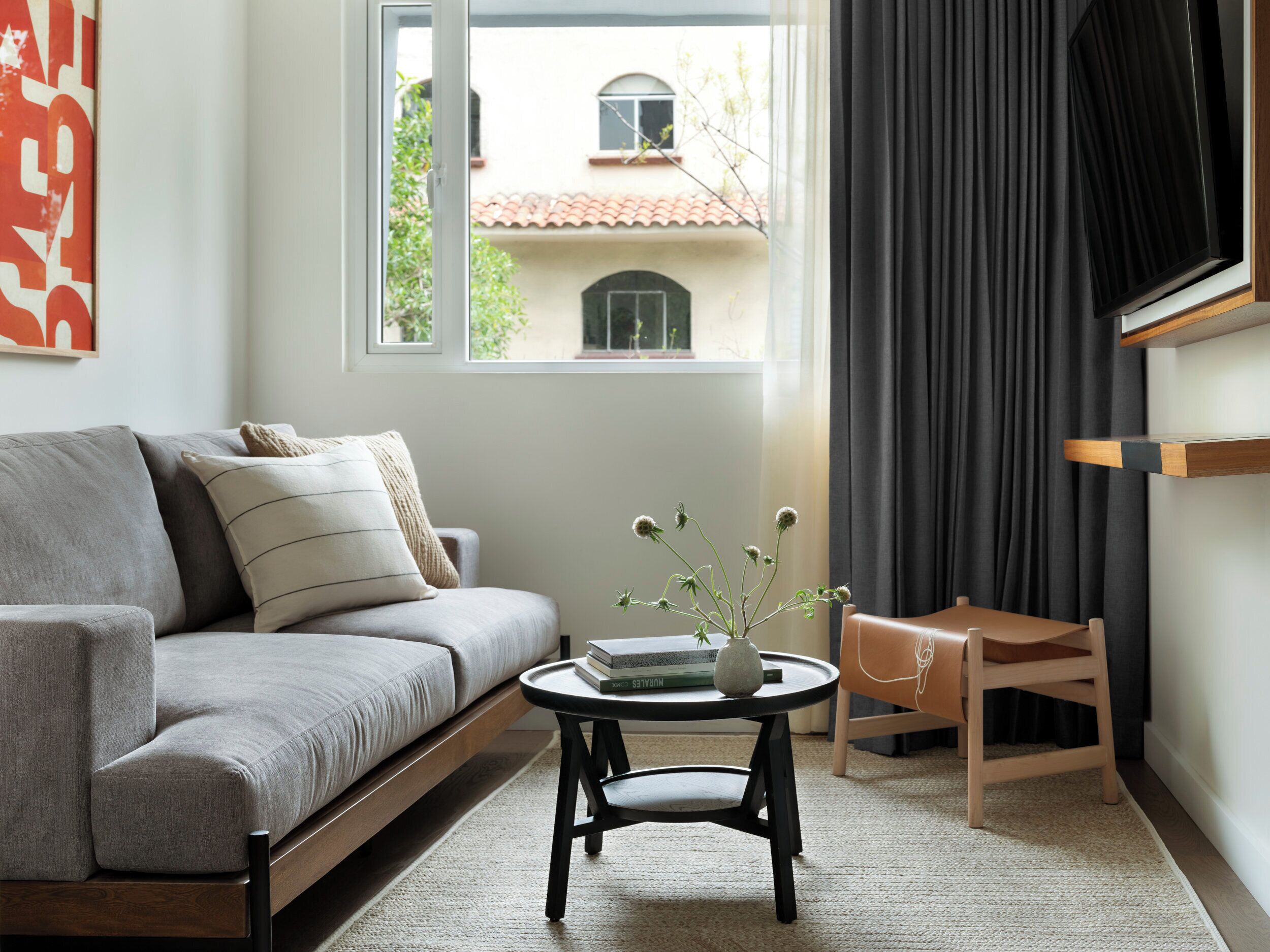 Una sala de estar moderna con un sofá gris, una mesita redonda y vistas a un edificio a través de una ventana.