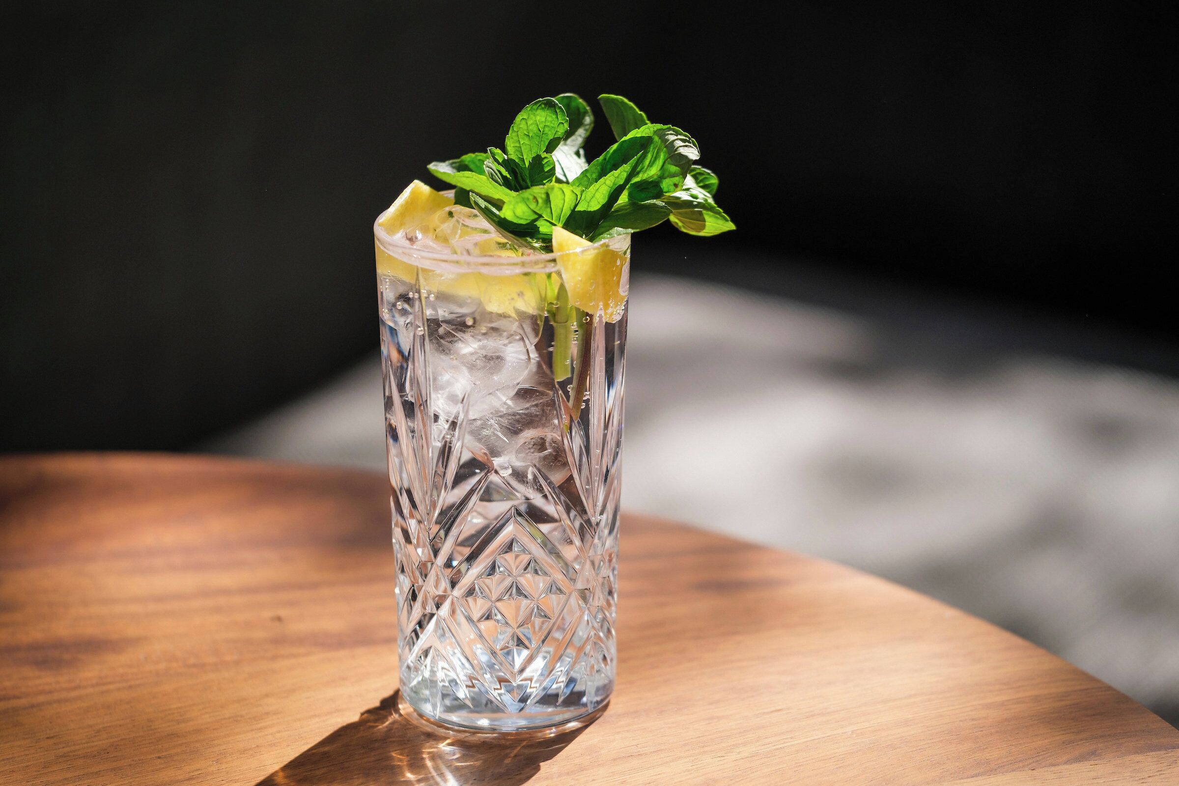 Un vaso transparente con cubitos de hielo y hojas de menta sobre una mesa de madera.