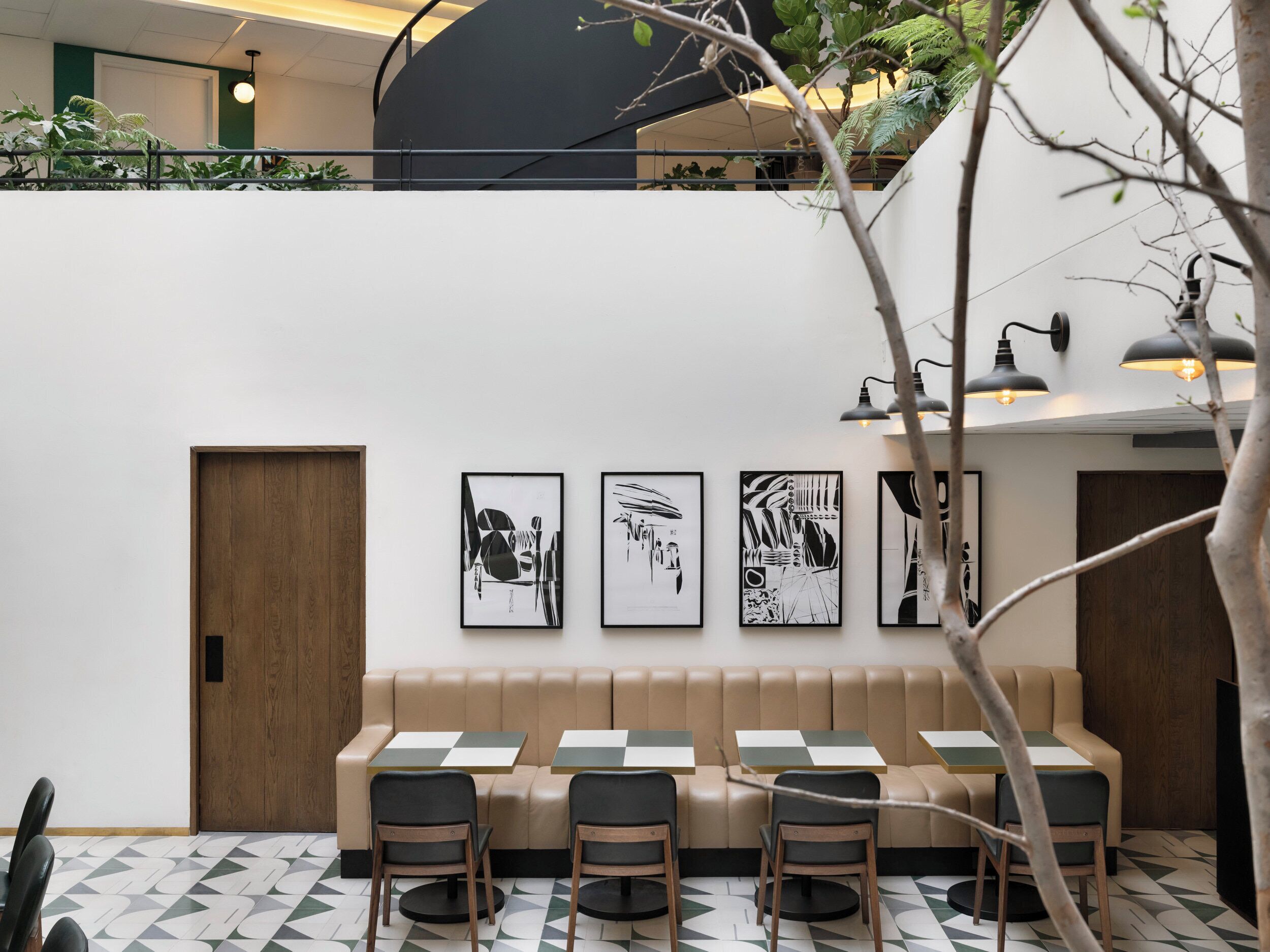 A modern interior with a high ceiling, a seating area with tables and chairs, and artwork on the walls.