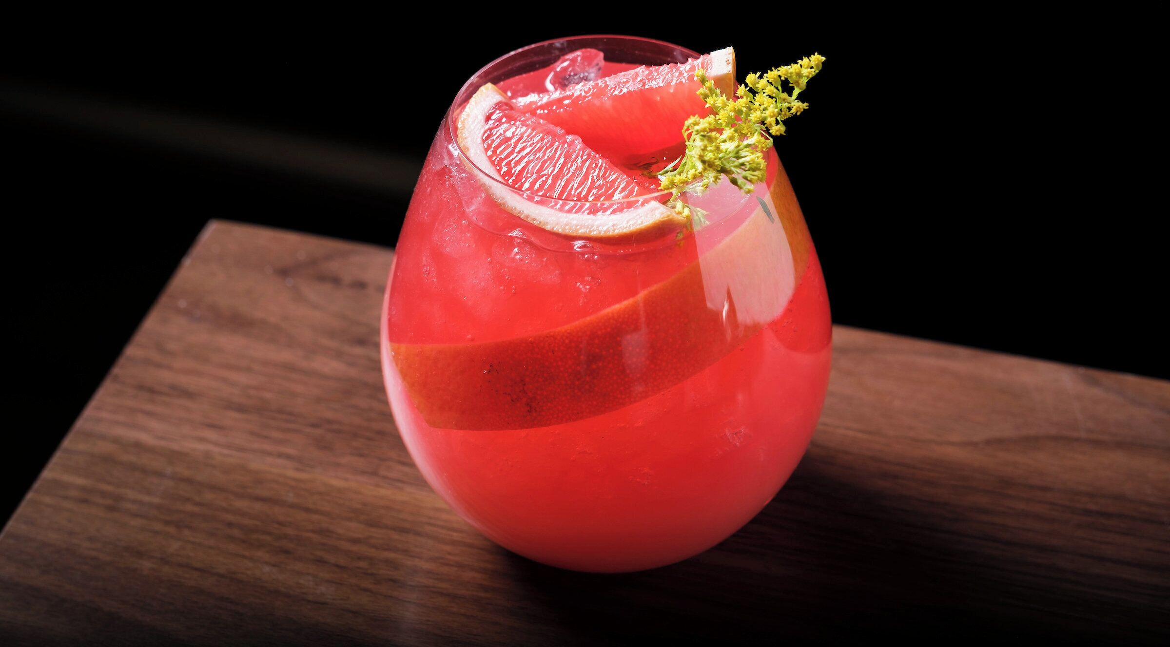 A cocktail in a glass with a slice of citrus and a garnish on a wooden surface.