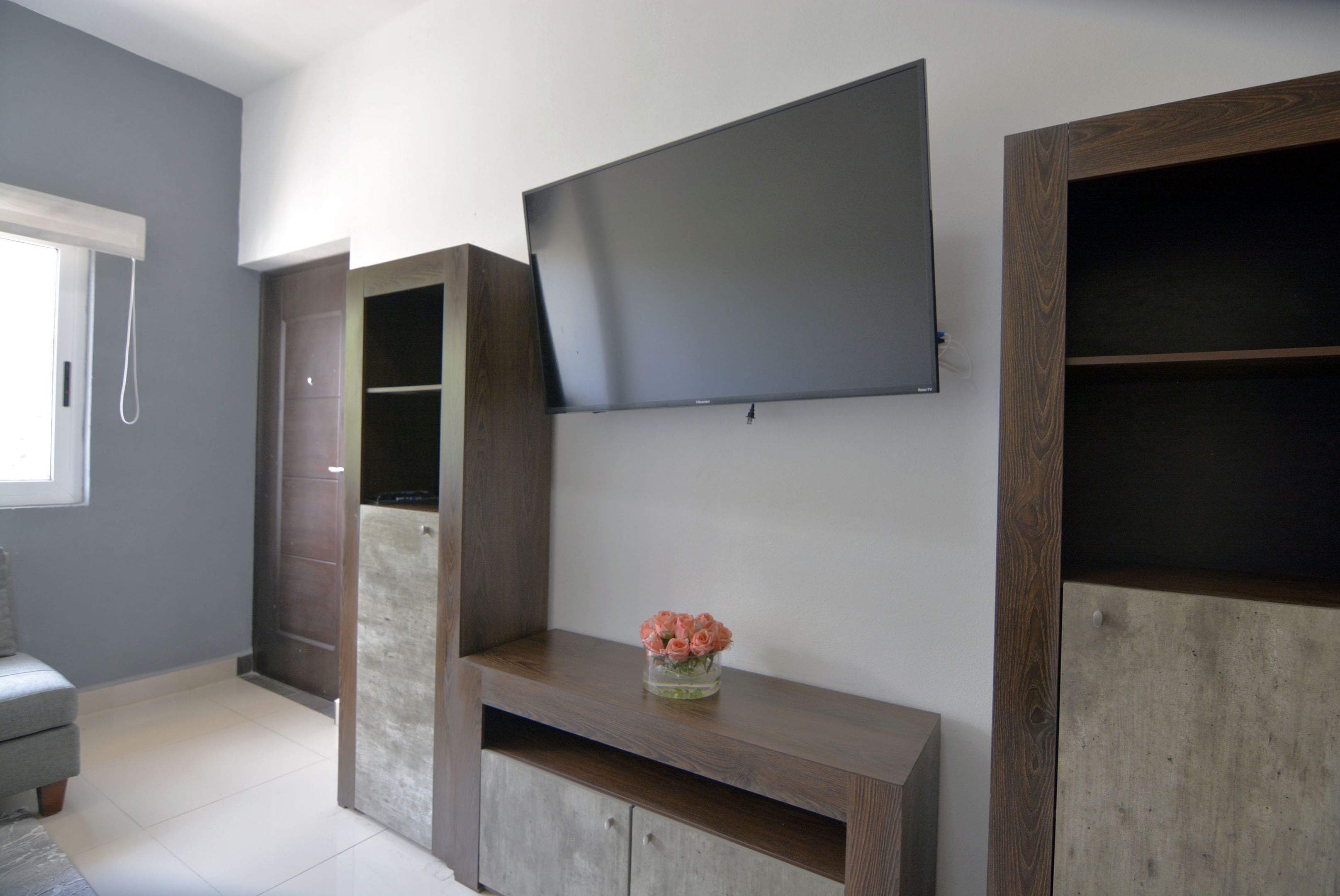 A modern living room with a flat-screen TV mounted on the wall, a built-in entertainment unit, and a small vase with flowers on a shelf.