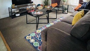 A living room with a flat-screen TV, a ceiling fan, a sofa, a coffee table, and a patterned rug. - The Shotgun House. (Silverton)