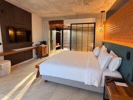 A modern bedroom with a large bed, a TV, a wooden bench, and a brick wall.