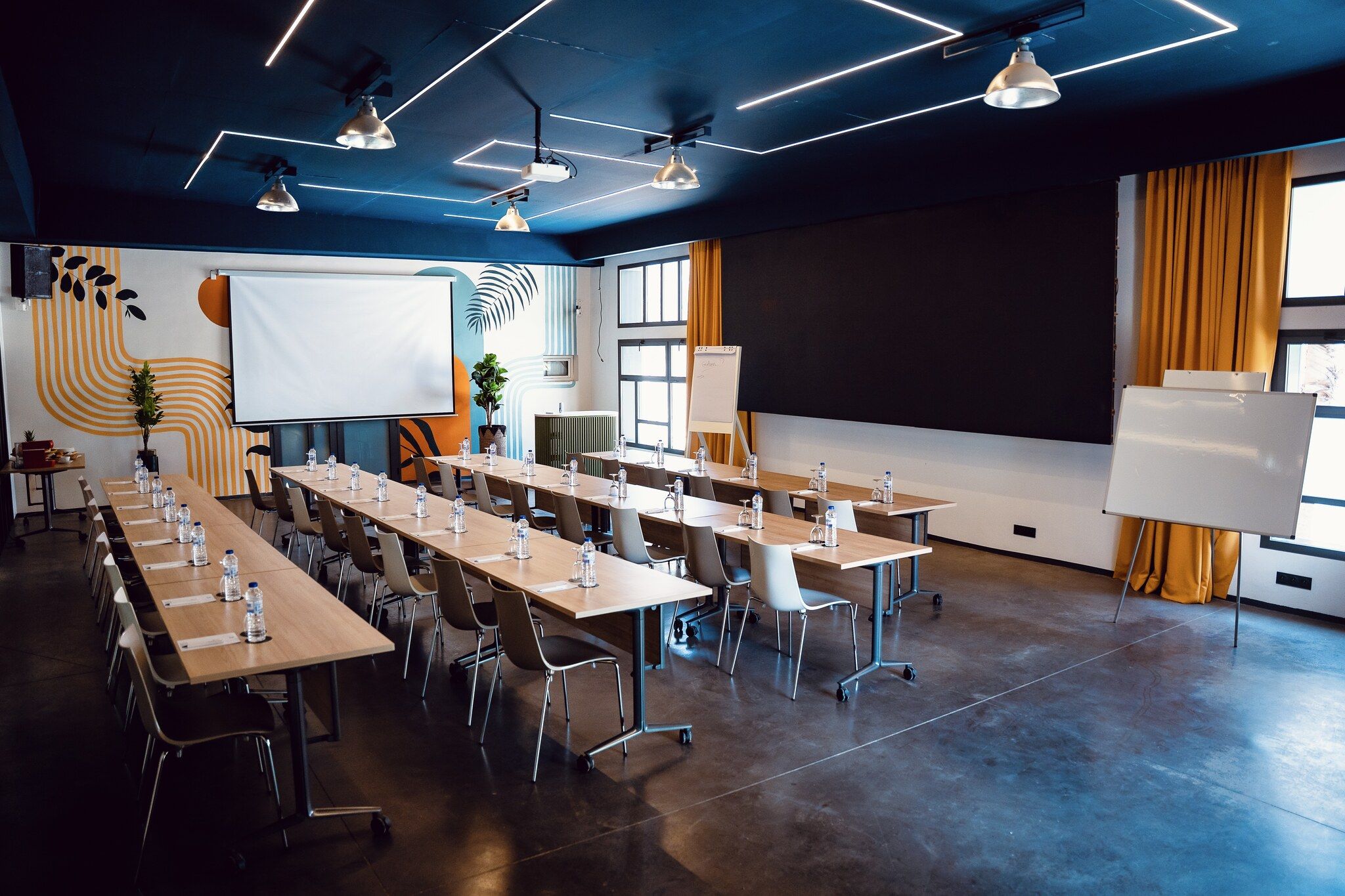 Une salle de conférence équipée d’une longue table, de chaises, d’un écran de projection et d’un tableau blanc.