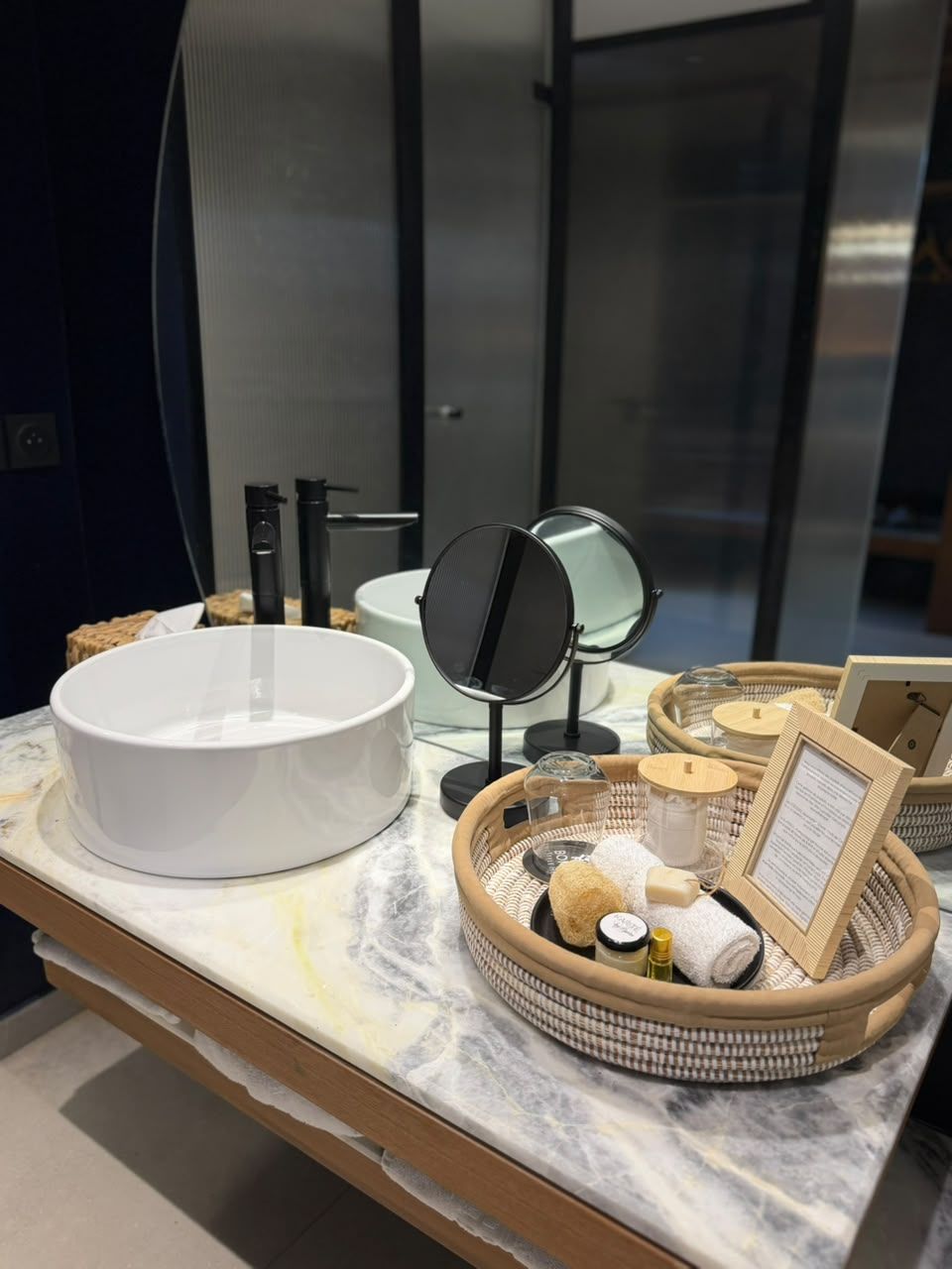 A bathroom vanity with a white basin, a round mirror, and a tray with toiletries.