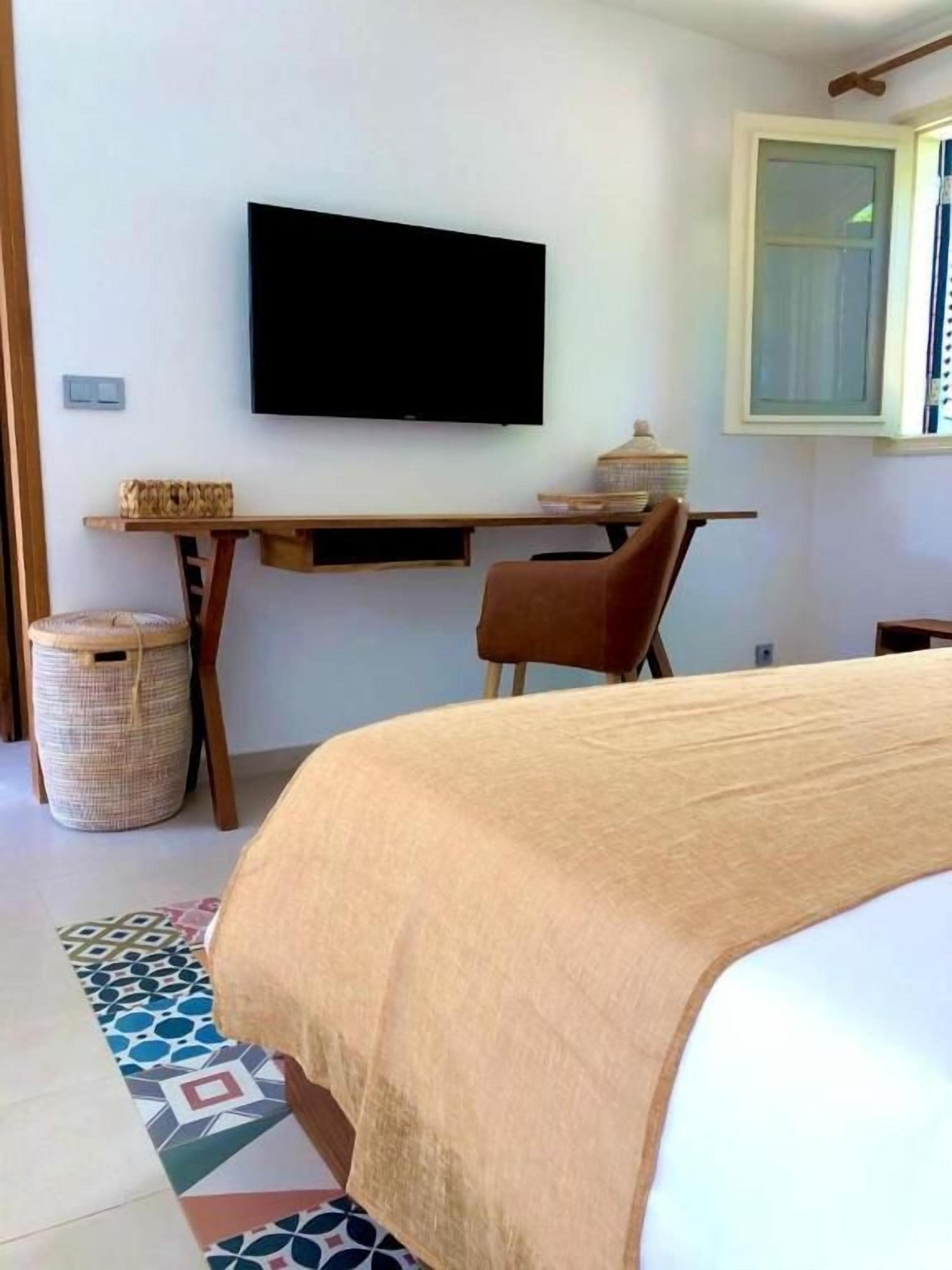 A bedroom with a bed, a desk, a television, and a window.