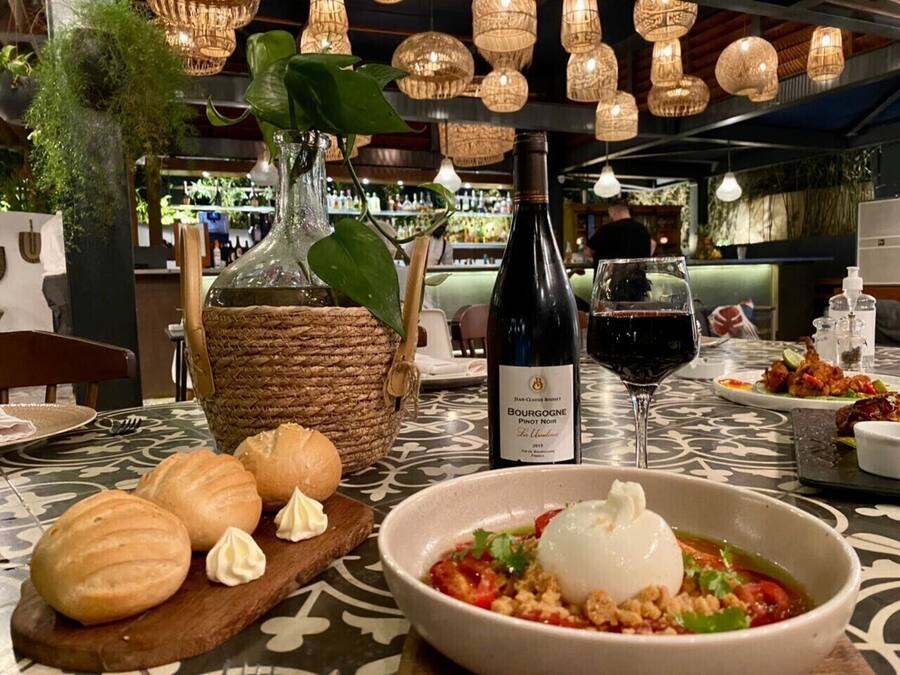 A dining table with a bottle of wine, bread, and a bowl of soup.