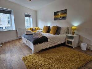 A bedroom with a bed, a nightstand, a lamp, a window, and a painting on the wall. - Charming 1-bed Apartment in Cromer Town Centre (Cromer)
