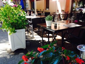 An outdoor dining area with tables and chairs, potted plants, and a wooden deck. - Hôtel Restaurant Les Marronniers (Thueyts)