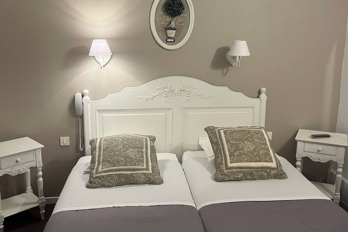 Una cama doble con dos almohadas, una mesita de noche, una lámpara y un adorno en la pared.