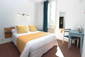 A hotel room with a bed, a desk, a chair, a mirror, and a window with curtains. - Hôtel Restaurant Les Marronniers (Thueyts)