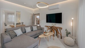 A modern living room with a grey sectional sofa, a wooden coffee table, and a mounted flat-screen TV. - Athena Luxury Villa by Estia (Gazi)