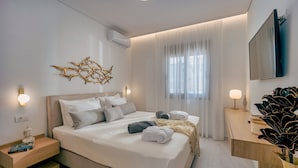 A modern bedroom with a large bed, bedside tables, a flat-screen TV, and a decorative wall piece. - Athena Luxury Villa by Estia (Gazi)