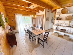 Un intérieur en bois comprenant une table à manger et des chaises, un lustre et des étagères ornées d’objets décoratifs.