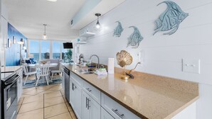 A modern kitchen with a large island, white cabinets, and decorative fish wall art. - Beachfront 2BR | Private Balcony, Pool | Gulf Views (Gulf Shores)