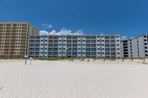 Ein Hotel direkt am Strand mit mehreren Etagen, Balkonen und einem sandigen Strand im Vordergrund.