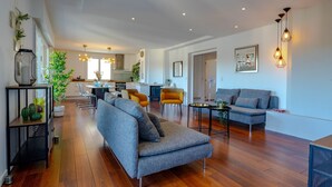 Un espacio habitable amplio con un sofá gris, una mesa de centro y una mesa de comedor. Se observan sillas y una cocina al fondo.