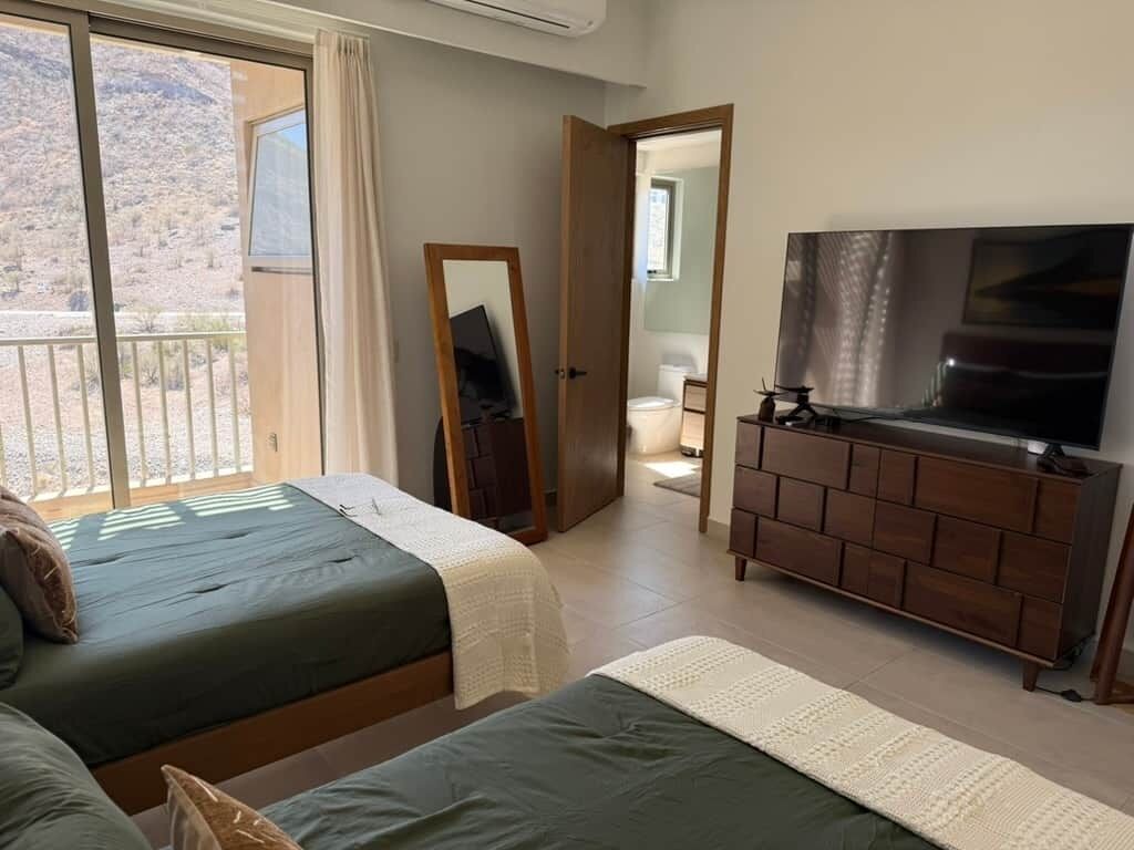 Un dormitorio con dos camas, televisión, cómoda y balcón con vistas a un paisaje montañoso.