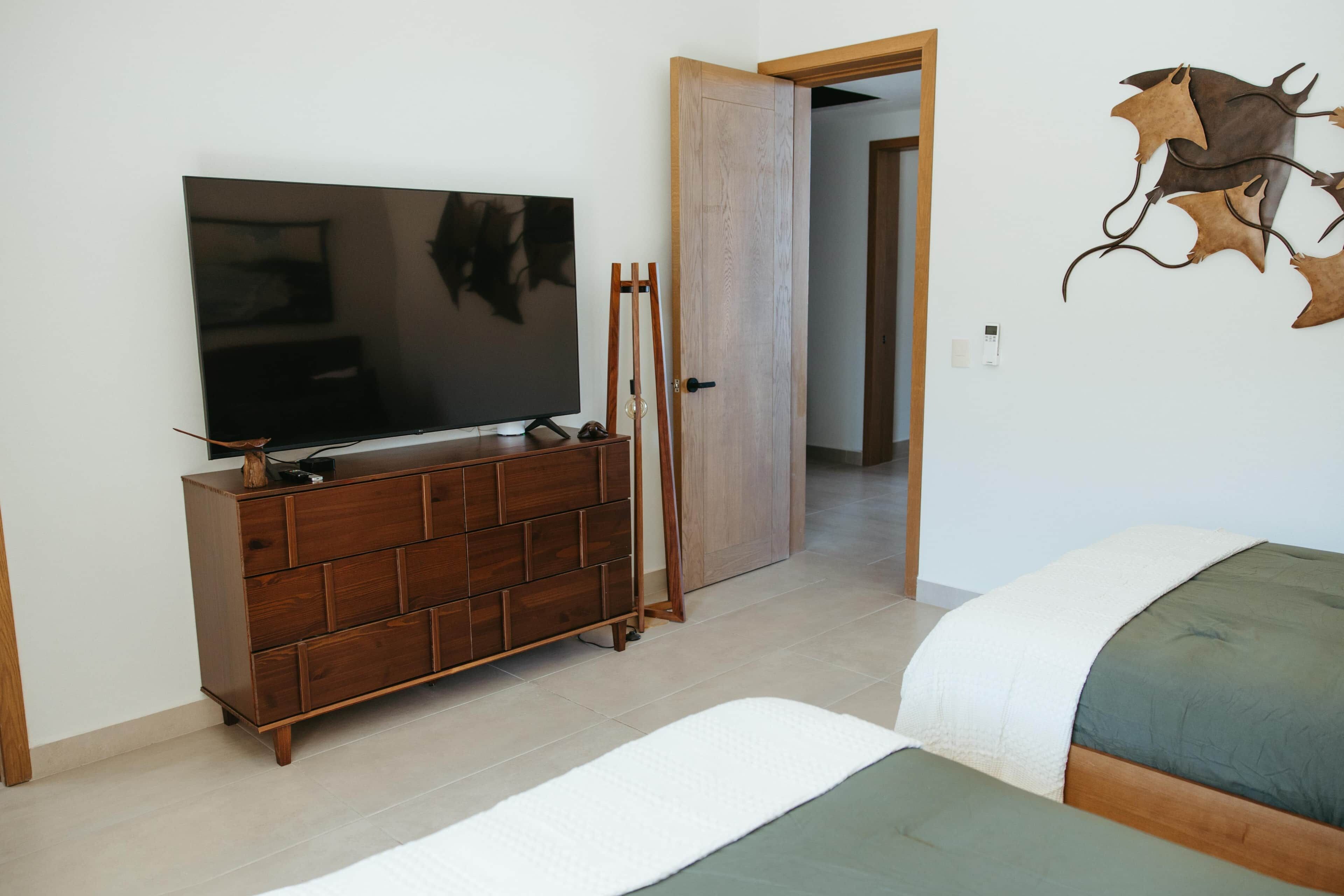 Habitación con televisor sobre una cómoda de madera, cama con ropa de cama verde y una obra de arte colgada en la pared.