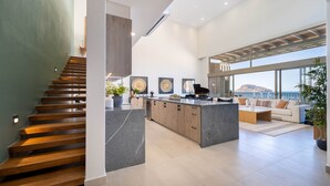 A spacious living area with a kitchen island, a staircase, and large windows offering a view.