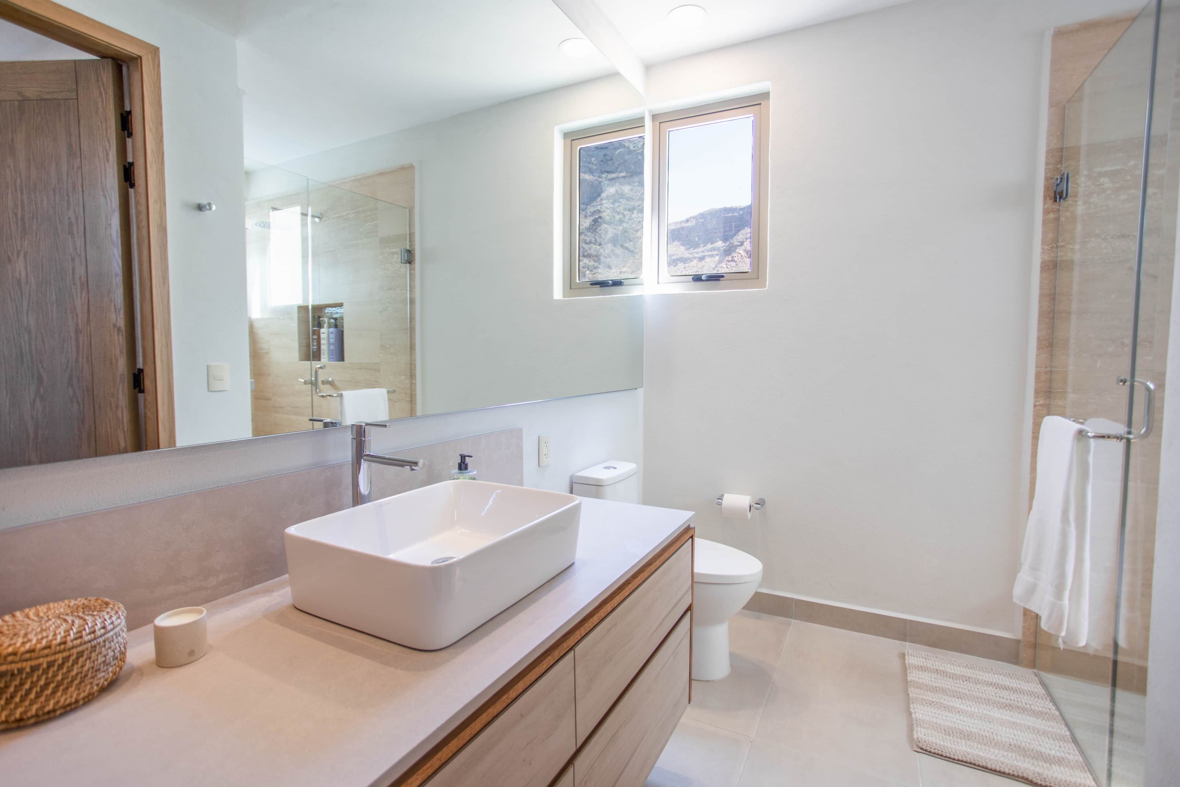 Ein modernes Badezimmer mit einem großen Spiegel, einem Aufsatzwaschbecken, einer Toilette und einer Duschkabine.