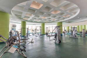Uma academia com diversos equipamentos de exercício, paredes verdes e teto com iluminação embutida.