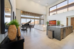 A spacious living area with a piano, a large window, a modern kitchen, and a balcony.