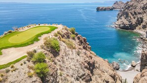 A coastal golf course with a clear view of the sea and rocky cliffs.