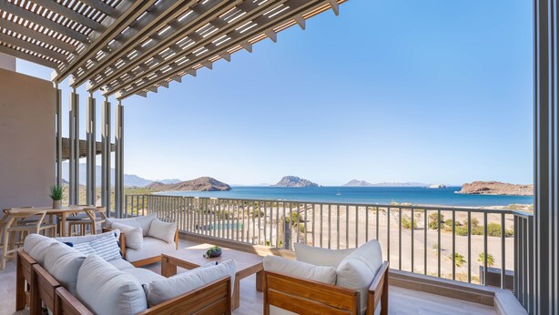 A balcony with a view of the sea, wooden furniture, and a pergola.