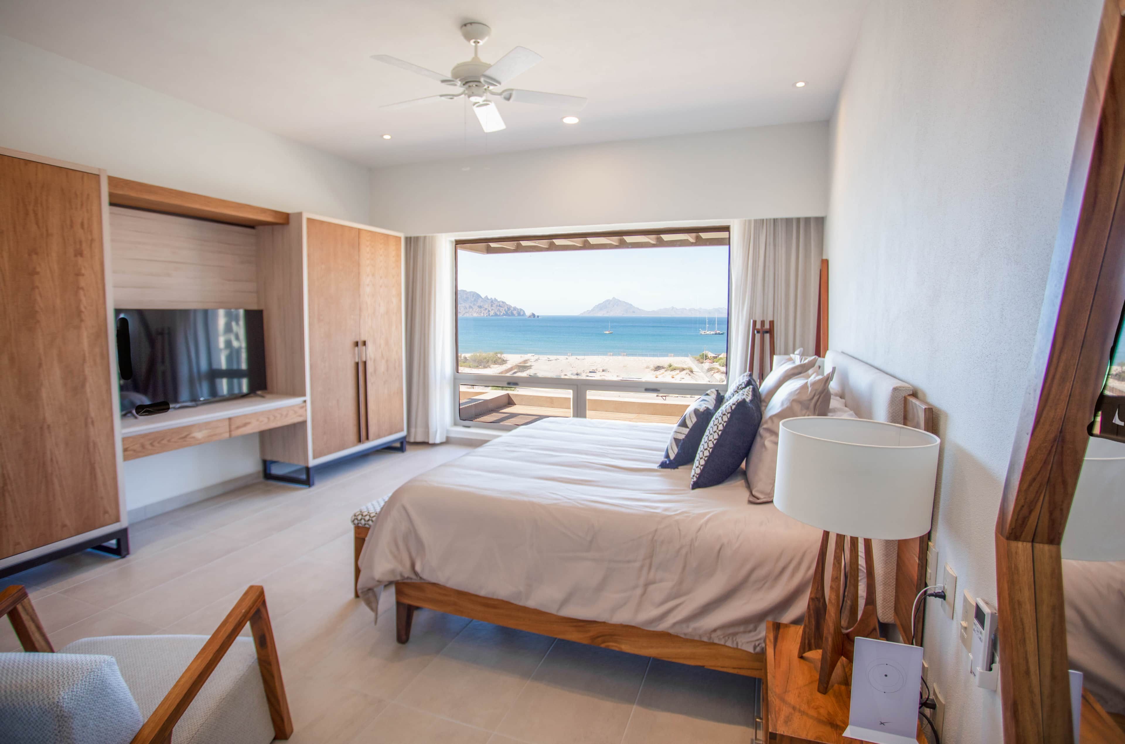 Une chambre avec un lit, une télévision, un ventilateur de plafond et une vue sur la plage.