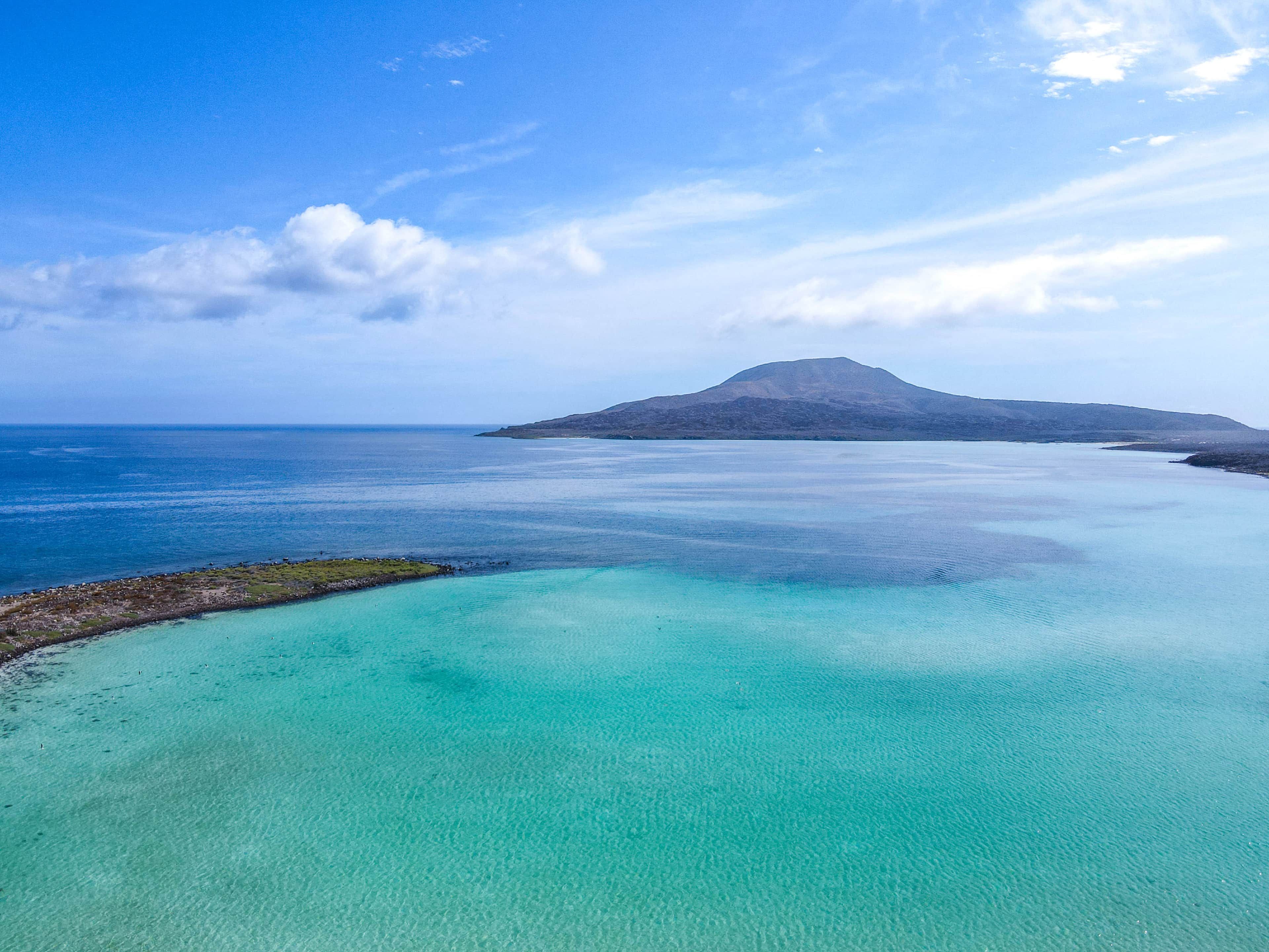 Eine Küstenlandschaft mit klarem türkisblauem Wasser, einem entfernten Berg und einer felsigen Küste.