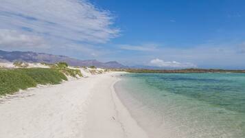 A beach with clear turquoise water, white sand, and distant mountains.