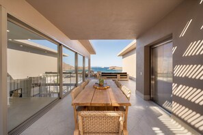 A modern outdoor dining area with a wooden table and wicker chairs, overlooking a scenic view. - 1604 4BR/5BA Oceanfront PH Loreto @ Danzante Bay (Ensenada Blanca)