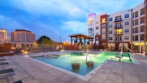 Uma área de piscina no terraço com espreguiçadeiras e um espaço de estar coberto, cercada por edifícios modernos.