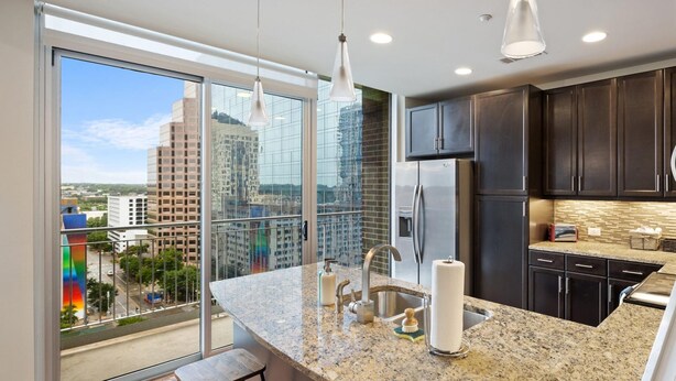 A modern kitchen with granite countertops, stainless steel appliances, and a large window offering a city view. - Austin Modern 1BD 1BA Apartment (Austin)